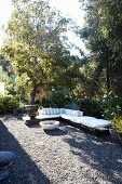 Corner bench with white cushions and fire bowl on sunny, gravel terrace in garden