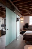 Glass partition with sliding door between bedroom and living areas in elegant loft apartment with rustic, wood-beamed ceiling
