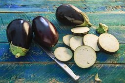 Whole aubergines and sliced aubergines on a rustic wooden table