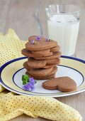 A stack of peanut butter and chocolate cookies shaped like hearts and stars with a glass of milk
