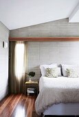 Doppelbett mit strukturierter Tagesdecke vor der weichen Textur einer hellgrauen Ziegelwand, Parkett aus der australischen Baumart Spotted Gum