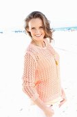 A young woman on a beach wearing an apricot coloured summer jumper