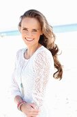 A young, long-haired woman on a beach wearing in a white lace dress