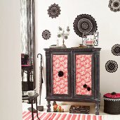 Make-over - vintage cabinet with fabric-covered, ethnic-style doors against wall decorated with black crocheted doilies