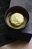 A cupcake with matcha tea frosting in a bowl on matcha powder