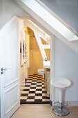 Vintage Barhocker neben offener Tür und Blick in ländliches Bad unter dem Dach, schwarz-weisser Schachbrettmusterboden