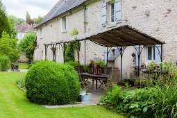 Terrassenplatz mit Metallpergola vor Naturstein-Landhaus und Garten