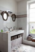 Masonry washstand with twin sinks below round mirrors in renovated bathroom with cement floor tiles
