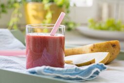 A strawberry and pear smoothie in a glass with a straw