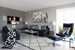 Grey-painted lounge area with black sofa and chairs around delicate coffee table on rug