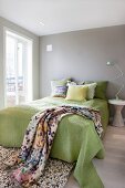 Green bedspread and scatter cushions arranged on double bed and classic table lamp on bedside table in bedroom painted pale grey