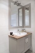 Waschtisch mit grau lackiertem Unterschrank und gerahmter Spiegel oberhalb Wandleuchte in Badezimmerecke