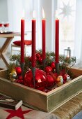 An advent's wreath in a wooden box with red baubles and four red, burning candles
