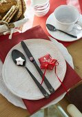 A folded red paper as a place card on a white plate with cutlery next to a cup and saucer