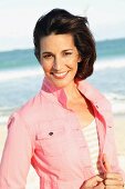 A brunette woman wearing a short pink denim jacket on the beach
