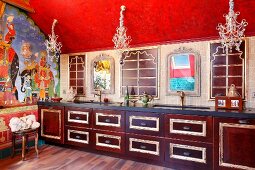 Kitchen with Indian-style decor - wooden base units with gilt mouldings in long kitchen counter below delicate chandeliers hanging from red ceiling