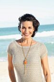 A dark-haired woman on a beach wearing a short-sleeved summer jumper