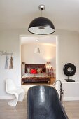 Grey, free-standing bathtub with floor-mounted taps in minimalist bathroom with white classic chair next to open doorway with view of country-style double bed