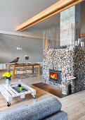 Back of sofa with grey marl cover, low coffee table made from white-painted pallet on castors and fireplace in gabion cage in modern interior