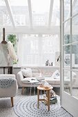 View through open door of round crocheted rug, fifties-style armchair and sofa in bright conservatory