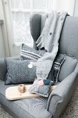 Felt scatter cushions, one embroidered, pin cushion and reel of thread on wooden board on grey armchair