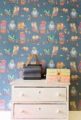 Portable, retro radio and cardboard boxes on vintage chest of drawers against wallpaper with pattern of owls