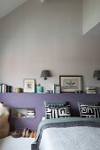 Modern bedroom with lilac headboard wall, stacked books, black and white pillows and vintage tailors' dummy