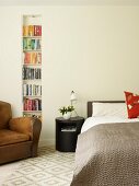 Brown leather armchair in front of bookcase in niche and black, cylindrical bedside cabinet next to bed