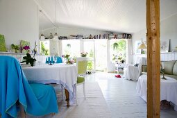 Light blue blanket draped over chair at table with tablecloth in open-plan cottage interior with white wooden floor