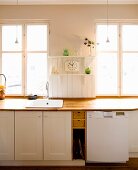 Kitchen counter with wooden worksurface and white cabinets below window in rustic interior