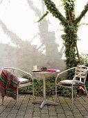 Seating area on terrace with bistro furnishings, paved floor and ivy-covered tree in courtyard