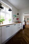 Kitchen counter with white base units below window in renovated period building with continuous herringbone parquet flooring