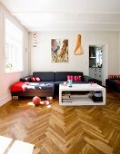 Wohnraum mit edlem Fischgrätparkett, moderner weißem Couchtisch und dunkelgrauer Sofakombination in renovierter Altbau Zimmerecke