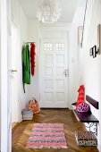 Blick durch offene Tür in Hausflur auf Teppichläufer und Fischgrätparkett, Garderobe und Holzbank an Wand montiert