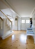 Foyer with polished wooden floor, bench opposite foot of white-painted wooden staircase and antique long-case clock in country house