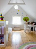 Kinderzimmer in ausgebautem Dach, seitlich Regal vor Matratze auf Dielenboden, im Hintergrund Kindertisch und Stühle an Giebelwand