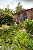 Lily pond amongst densely planted shrubs and trees in courtyard outside low brick building