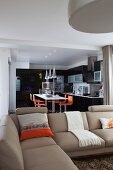 Beige sofa in front of open-plan fitted kitchen with black fronts and orange bar stools at counter