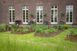 Raised beds with metal surrounds outside renovated, brick farmhouse