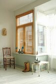 Old chair, side table, cowboy boots and pewter ornaments arranged next to window bay