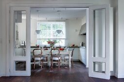 Country-house-style dining area with antique chairs at long table in white, modern kitchen-dining room