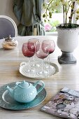 Weingläser aus rötlichem Rauchglas und Teekanne auf Esstisch