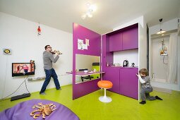 Father and son playing in multifunctional room with creative modular kitchen, beanbag in front of flatscreen TV and shower cubicle in background