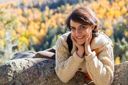 Woman wearing hiking gear lying on rock ledge in autumnal mountain landscape