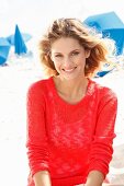 A young blonde woman on a beach wearing a transparent red knitted jumper