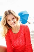 A young blonde woman on a beach wearing a transparent red knitted jumper