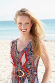 Blonde junge Frau in Sommerkleid mit Ethnomuster am Strand