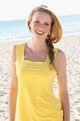 Blonde junge Frau in gelbem Sommerkleid am Strand