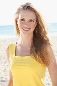 Blonde junge Frau in gelbem Top am Strand