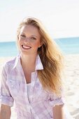 A young blonde woman on the beach wearing a purple and white checked blouse